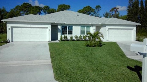 A white house with a grey roof and two garages.