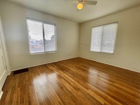 A room with wooden flooring and two windows.