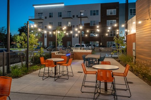 A patio with orange chairs and tables is set up in front of a building.