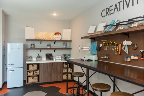 A kitchen area with a white fridge, a table with stools, and a shelf with various items.