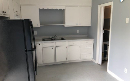A black refrigerator stands in a kitchen with white cabinets.