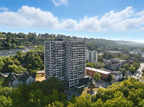 A tall building stands in the middle of a town with a river and trees in the background.