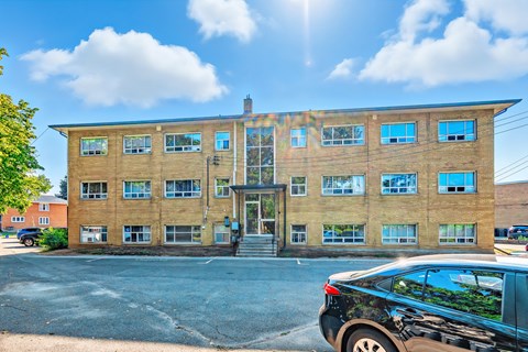 A black car is parked in front of a tan building with a glass door and windows.