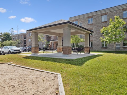 A sandbox is located in front of a building with a covered patio.