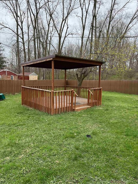A wooden gazebo with a brown roof is situated in a grassy backyard.