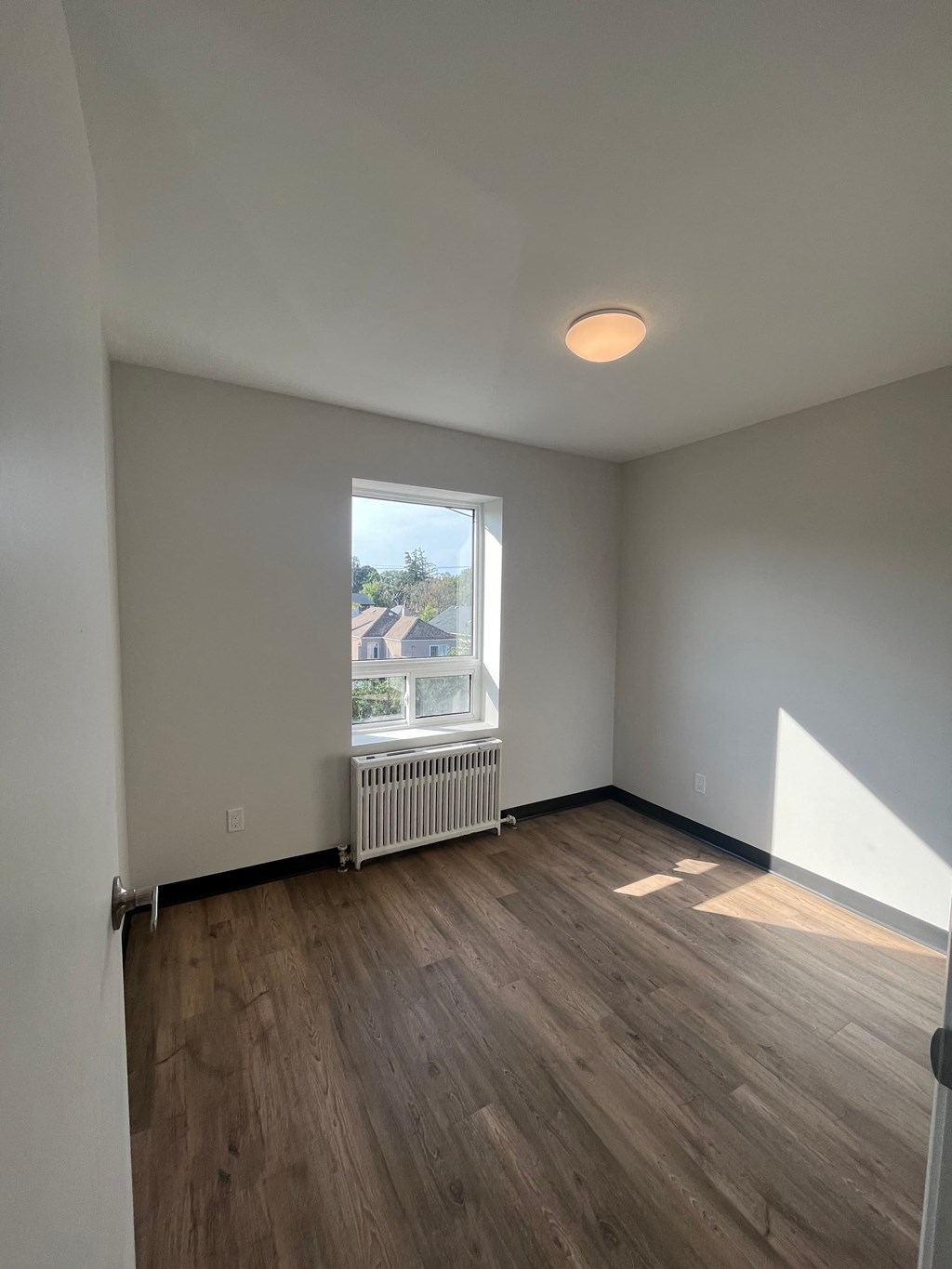 A room with wooden flooring and a window showing an outdoor view.
