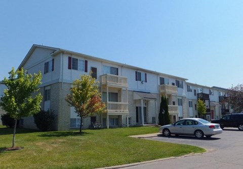 A silver car is parked in front of a white apartment building.