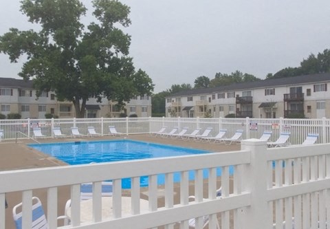 A pool surrounded by white chairs and a white fence.