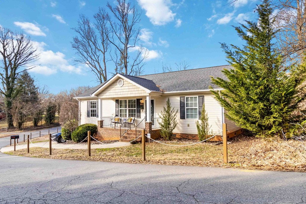 A house with a grey roof and a white exterior is surrounded by a fence and a tree.