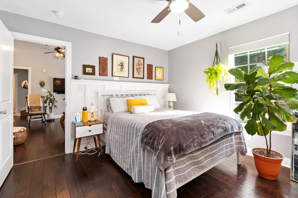 A bedroom with a bed, a plant, and a ceiling fan.