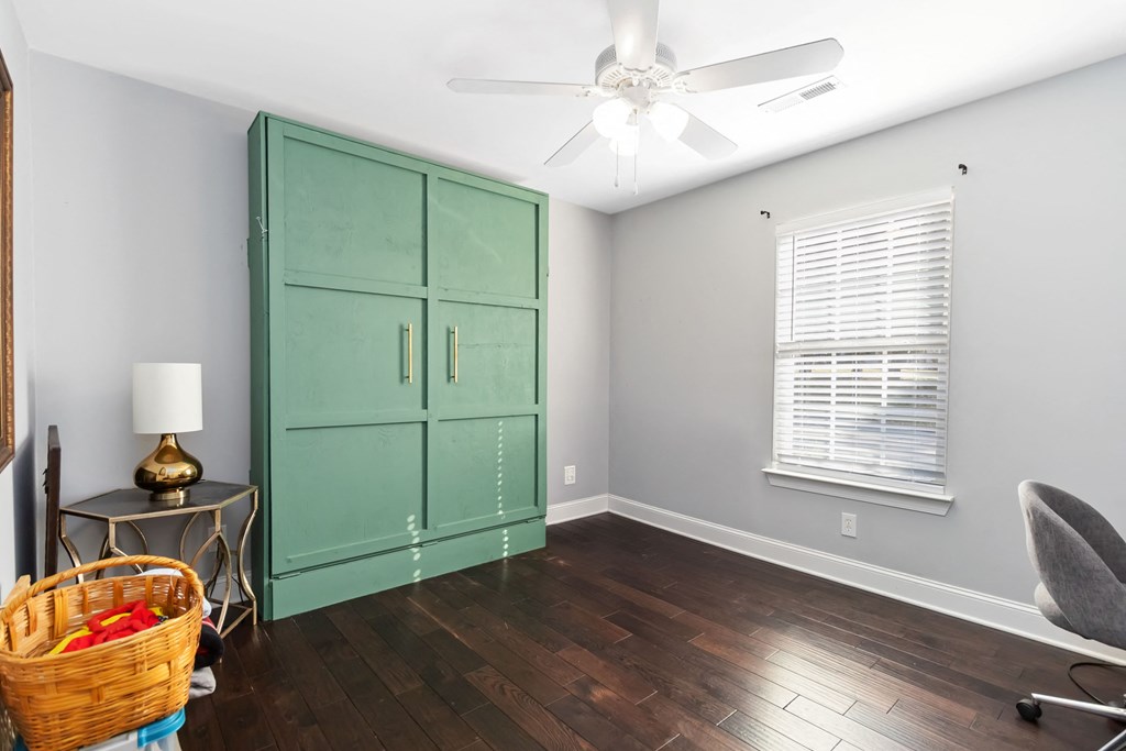 A room with a green cabinet, a ceiling fan, and a chair.