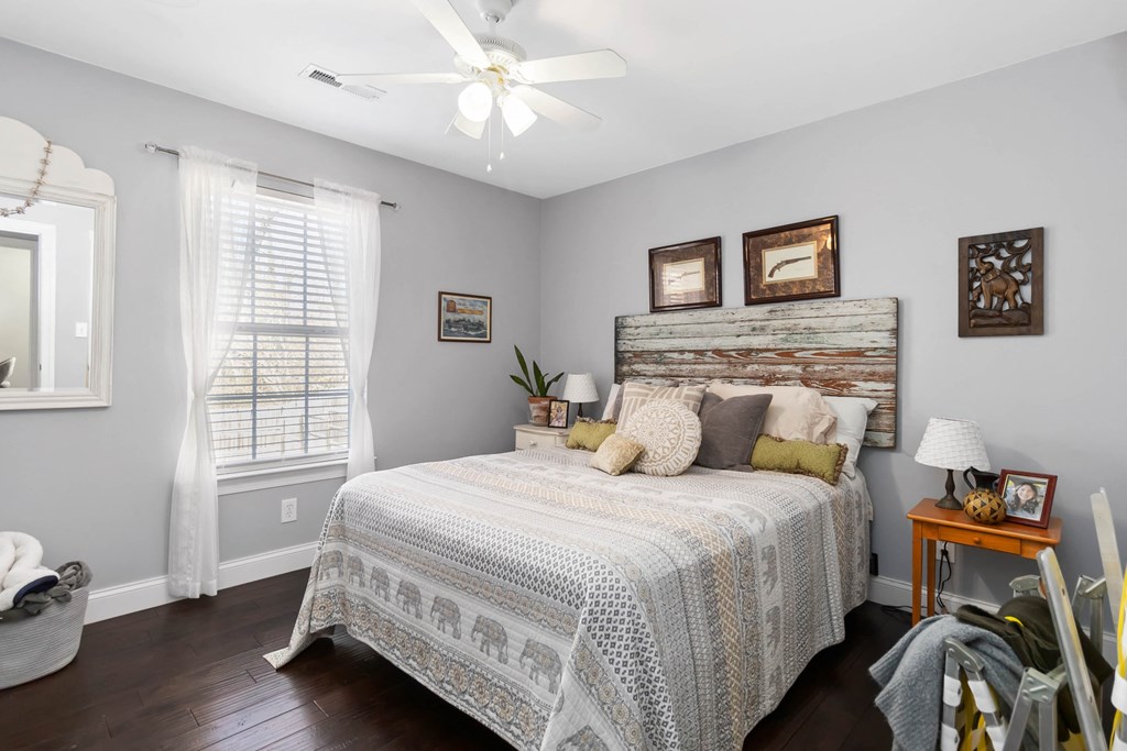 A bedroom with a bed, a ceiling fan, and a window with white curtains.