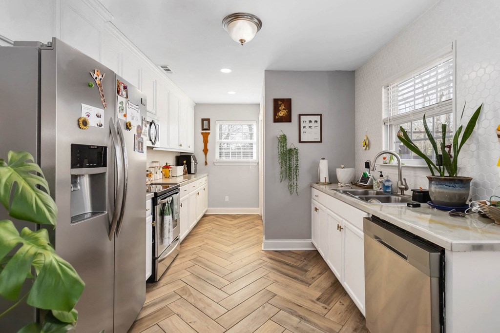 A kitchen with a refrigerator, sink, and wooden flooring.