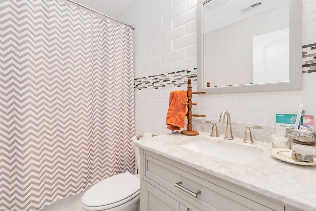A bathroom with a white toilet, a sink with a silver faucet, and a shower curtain with a chevron pattern.