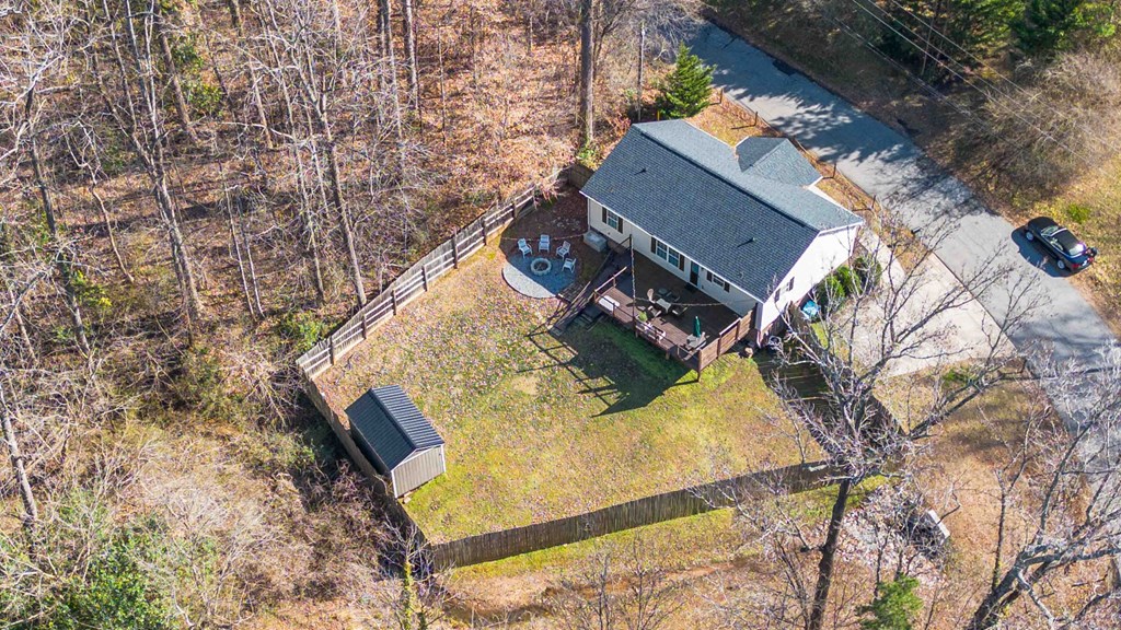 A house with a grey roof and a white garage door is surrounded by a fence and trees.