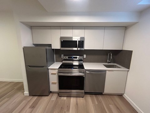 A modern kitchen with stainless steel appliances and wooden flooring.