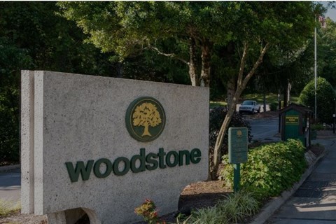 A sign for Woodstone is displayed in front of a tree-lined street.