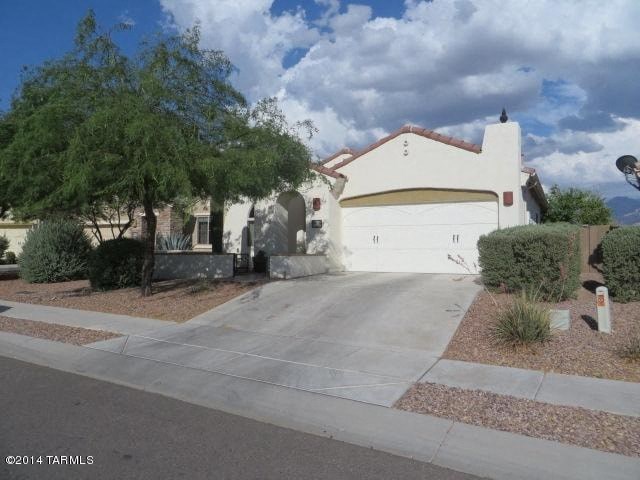 A white house with a driveway and a tree in front.