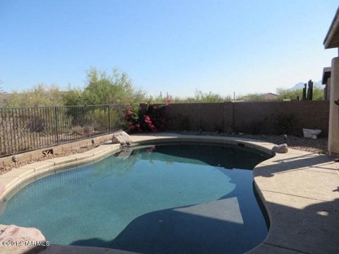 A small pool with a black fence and a wall with a flower bed.