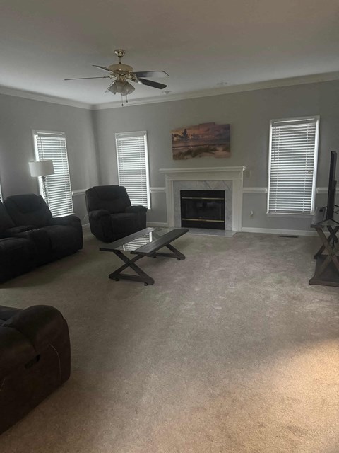 A living room with a fireplace, two chairs, and a ceiling fan.