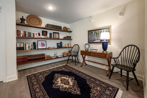 A room with a rug, a chair, a table, and shelves with books and decorative items.