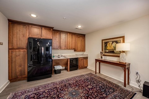 A black fridge sits in a kitchen with wooden cabinets and a rug on the floor.