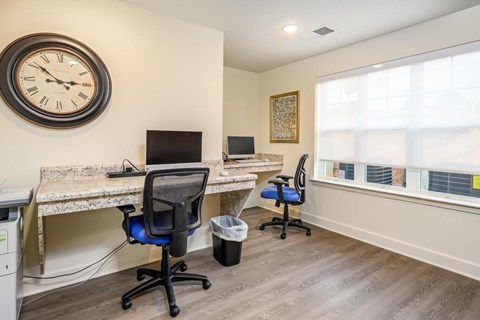 A room with a desk, chairs, and a clock on the wall.