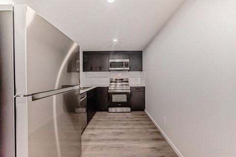 A modern kitchen with stainless steel appliances and a refrigerator on the left.