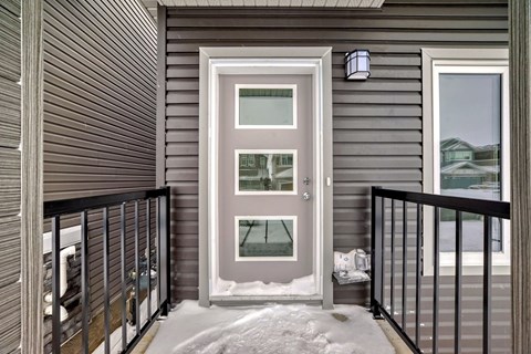 A grey house with a white door and a black railing.