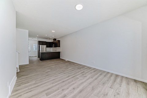 A spacious room with wooden flooring and a kitchen area in the background.