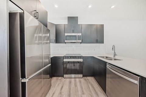 A modern kitchen with stainless steel appliances and wooden flooring.
