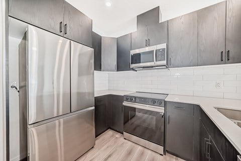 A modern kitchen with stainless steel appliances and a wooden floor.