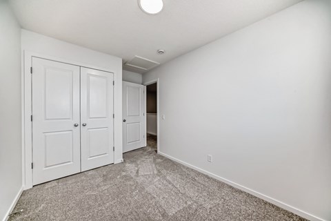 A room with white walls and a carpeted floor with a door on the left.