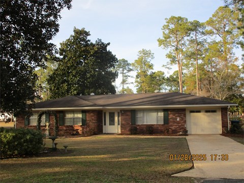 A house with a brick facade and a white garage door is surrounded by trees.