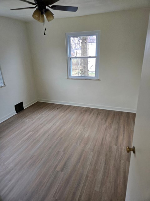 A room with a ceiling fan and a window with a view of trees.