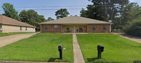 A house with a red brick exterior and a white door is surrounded by a green lawn.
