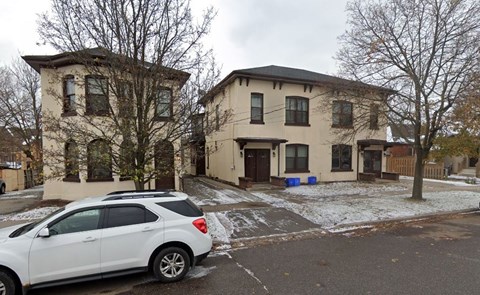 A white car is parked in front of a two-story building.