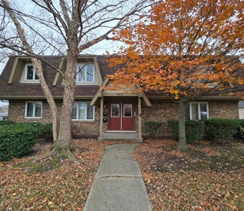 A house with a red door and a tree with orange leaves in front.