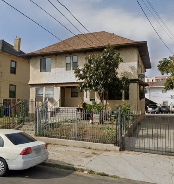 A white car is parked in front of a house with a black fence.