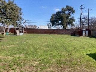 A large grassy field with a fence and trees in the background.