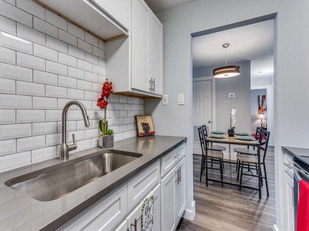 A kitchen with a white tile backsplash and a stainless steel sink.