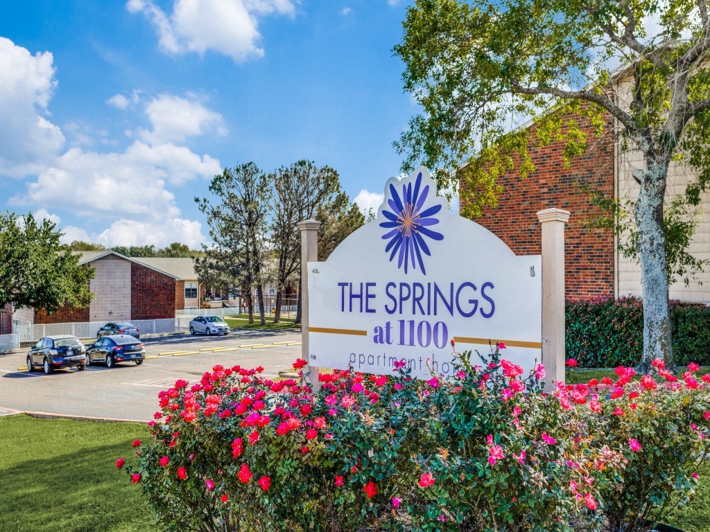 A sign for The Springs at 1100 is in front of a building and some trees.