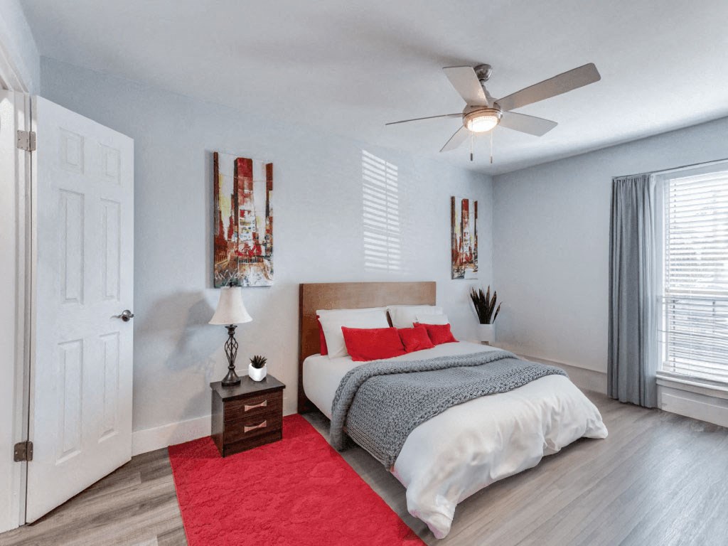 A bedroom with a bed, nightstand, and a red rug.