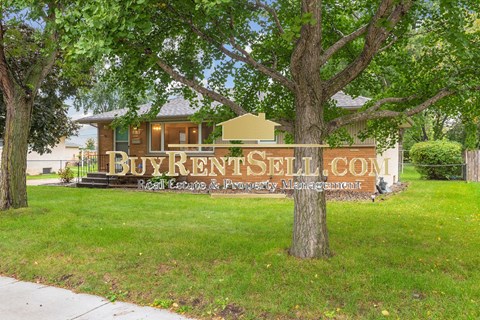 A sign that says BuyRentSell.com is in front of a house.