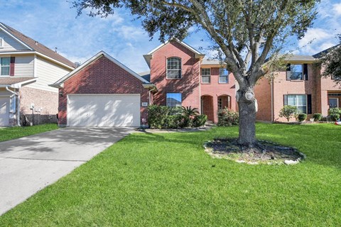 A tree in a grassy area in front of a red brick house.