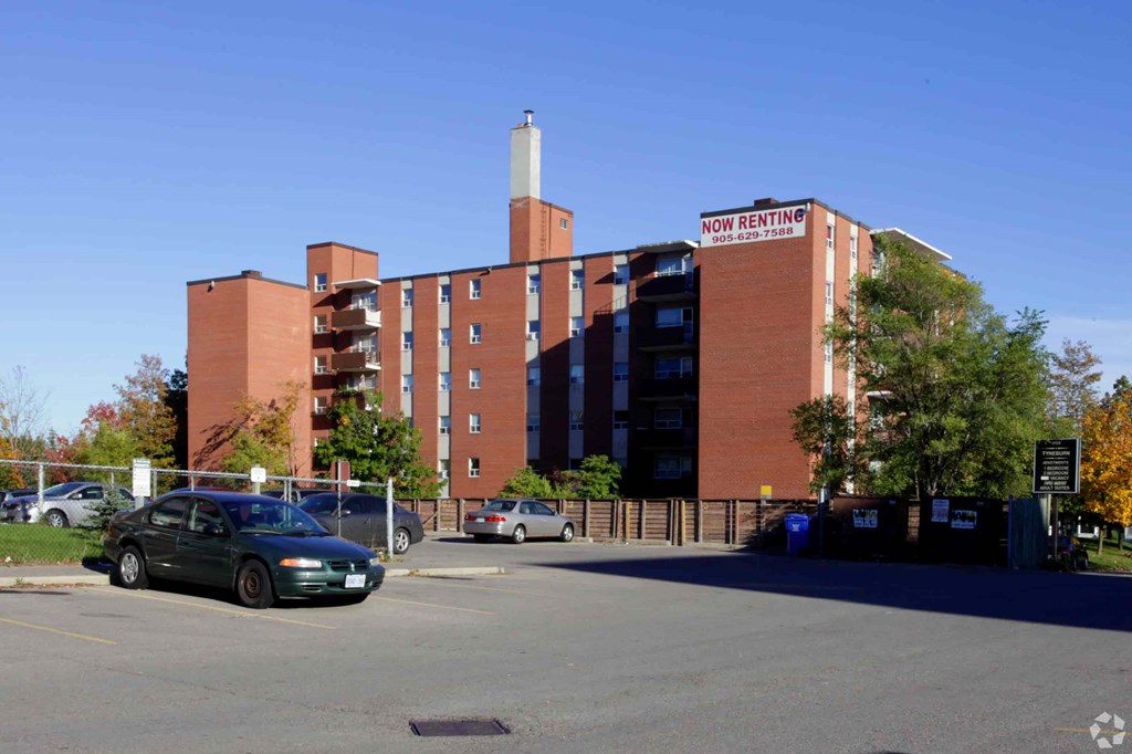 A car is parked in a parking lot in front of a brick building with a sign that says "Now Renting.".