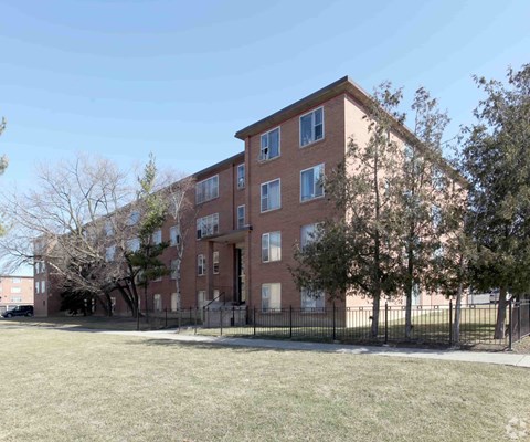 A large brick apartment building with a black fence in front.