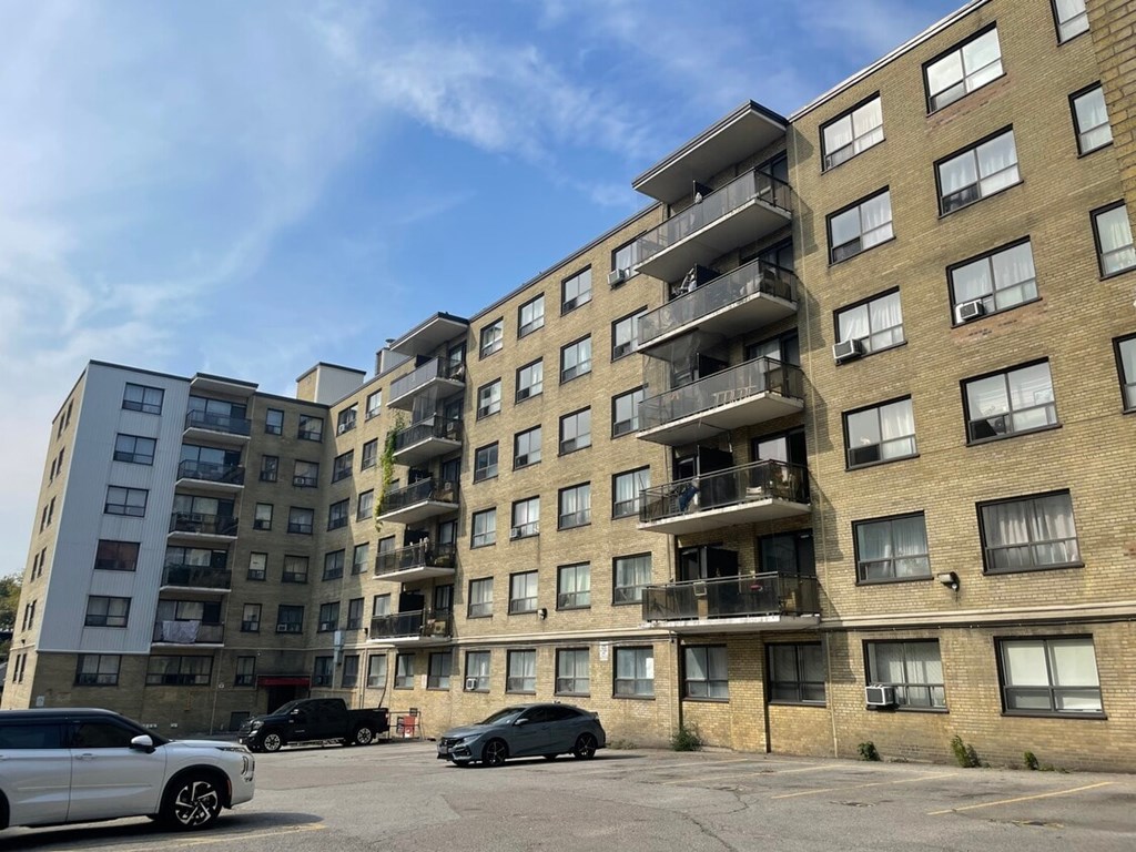 A white car is parked in front of a building with a balcony.
