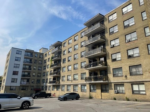 A white car is parked in front of a building with a balcony.