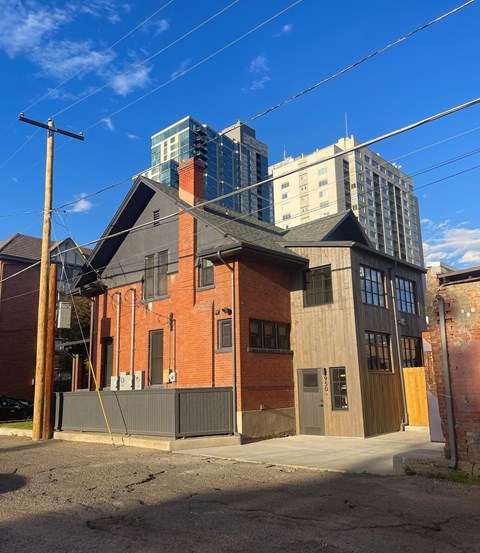 A red brick building with a black roof and a grey fence in front of it.
